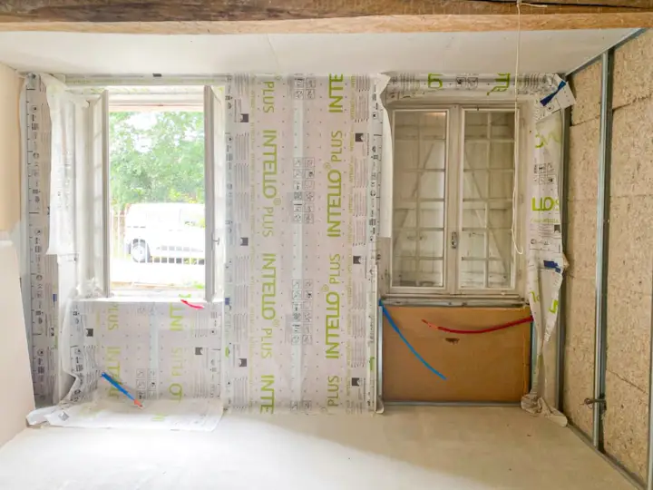 Pose de pare-vapeur pour comment isoler un mur intérieur. Fenêtres, tuyaux et ossature métallique visibles.