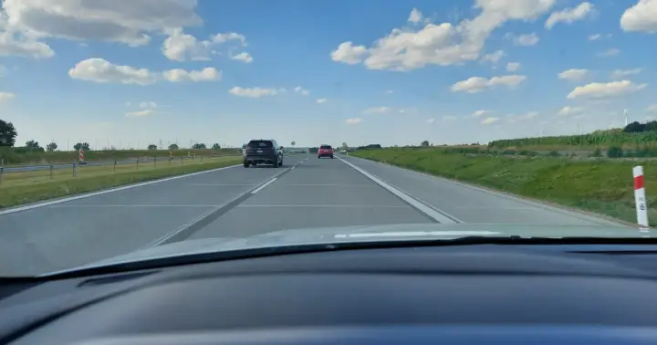 Jadąc na S7, widzimy pola i chmury. Samochody poruszają się po pustej drodze.