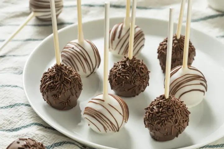 Pyszne cake pops przepis na talerzu: czekoladowe z posypką i białe z polewą.