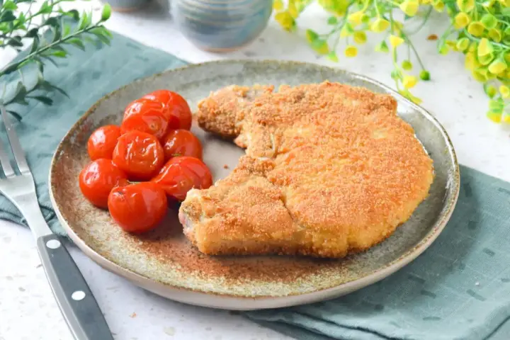 Cotoletta alla milanese dorada y crujiente, acompañada de tomates cherry asados. Un plato clásico y delicioso.