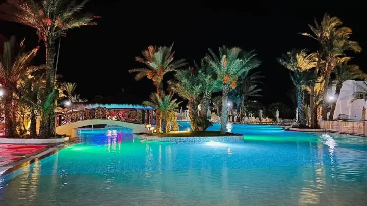 Nocny basen z palmami i mostkiem, idealne miejsce na relaks. Wiele pozytywnych fiesta beach djerba opinie potwierdza jego urok.