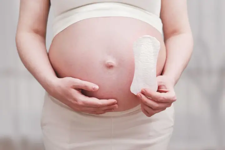 Ciężarna kobieta trzyma podpaskę, sugerując pytanie: czy w okres można zajść w ciążę?