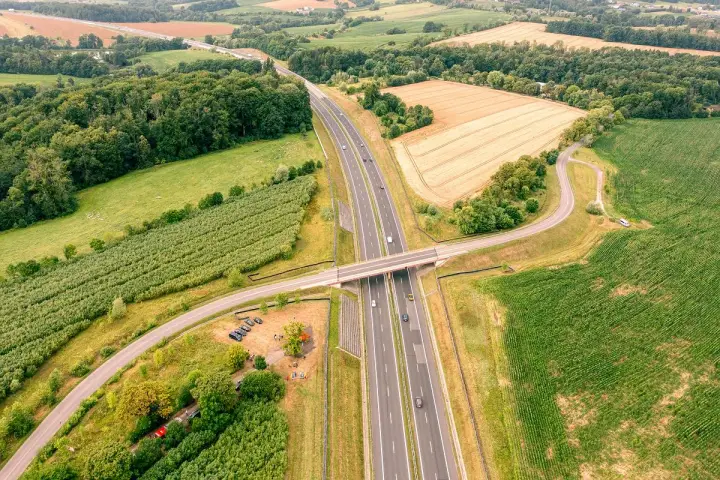 Nowa sól trasa przecina zielone pola i lasy, łącząc odległe zakątki. Widok z lotu ptaka ukazuje drogę, most i samochody w ruchu.