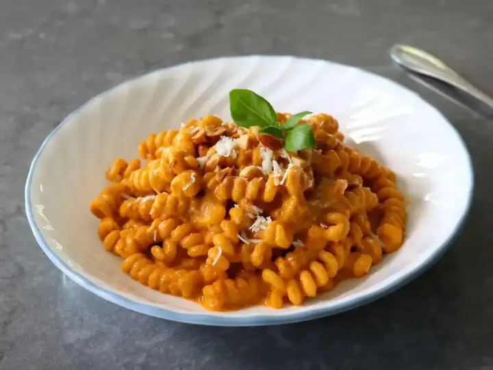 Szybki obiad z makaronem fusilli w kremowym sosie pomidorowym, posypany parmezanem i orzechami, udekorowany listkiem bazylii.