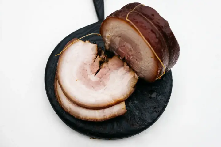 Pokrojony boczek chashu, z widocznymi warstwami mięsa i tłuszczu, ułożony na ciemnej desce.