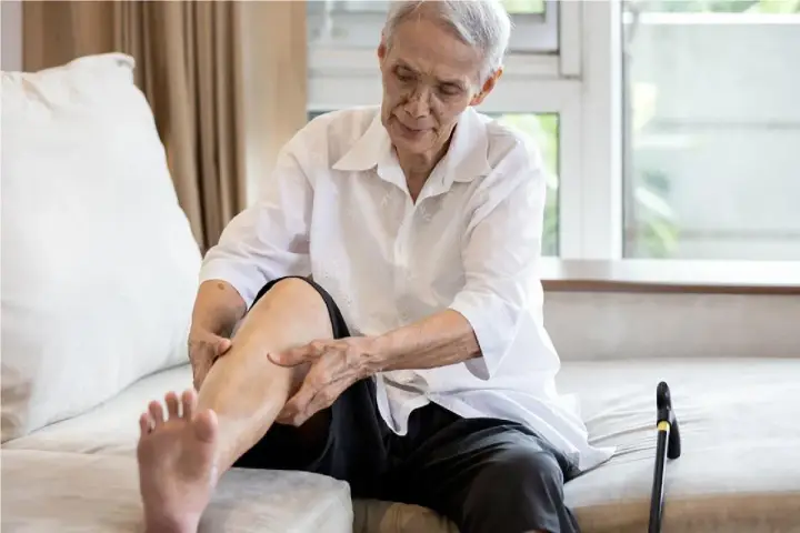 Anziano con gambe gonfie cerca rimedi, massaggiando la caviglia.