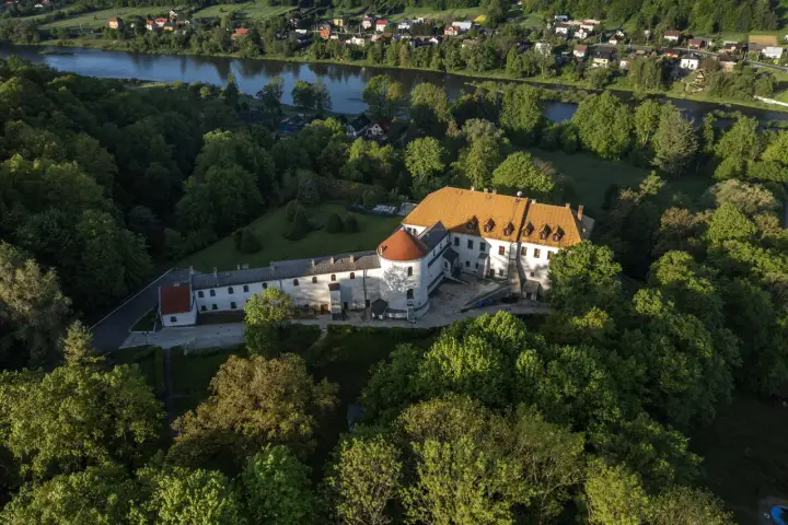 Zamek w Lesku otoczony zielenią, z widokiem na rzekę i miasteczko.