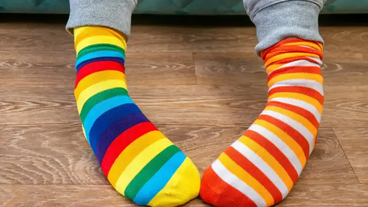 Kolorowe skarpetki w paski, tęczowe i pomarańczowo-białe, leżą na drewnianej podłodze. Jak doprać kolorowe skarpetki?