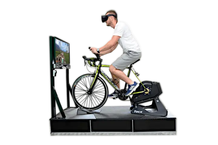 Mężczyzna w goglach VR pedałuje na rowerze stacjonarnym, doświadczając wirtualnej przejażdżki. To zaawansowany symulator jazdy rowerem.