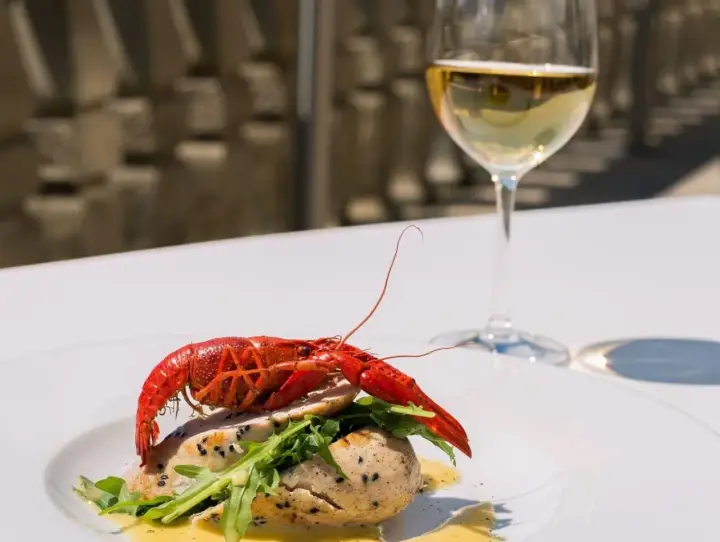Un plat de poisson avec une écrevisse rouge, roquette et sauce, accompagné d'un verre de chenin blanc sec ou moelleux.