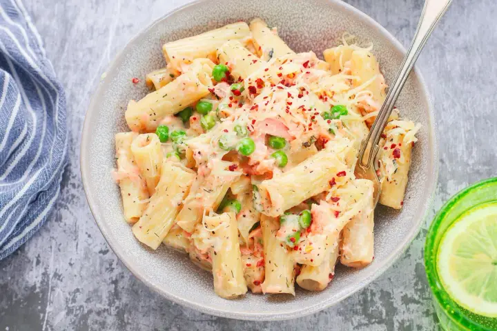 Pyszne danie z makaronem rigatoni, kawałkami łososia, groszkiem i kremowym sosem, posypane serem i płatkami chili. Idealna pasta z łososia na obiad.