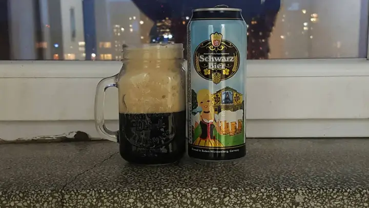 Perlenbacher Schwarz Bier w kuflu, obok puszka piwa. Wieczorny widok na miasto w tle.