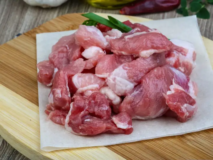 Surowe, pokrojone w kostkę mięso wieprzowe, idealne na gulasz. W tle czosnek i papryczki chili.