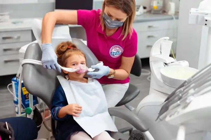Dziecko w masce do sedacji wziewnej. Dentystka monitoruje stan pacjenta, minimalizując potencjalne skutki uboczne.