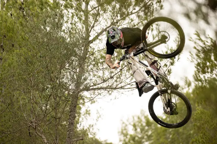 Tomas Lemoine fliegt mit seinem Mountainbike durch die Luft, umgeben von Bäumen.