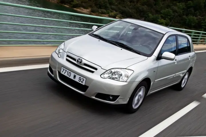 Srebrna Toyota Corolla 2004 na moście, z widokiem na wodę i las.