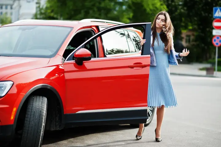 Mujer elegante sale de un monovolumen o SUV rojo brillante.