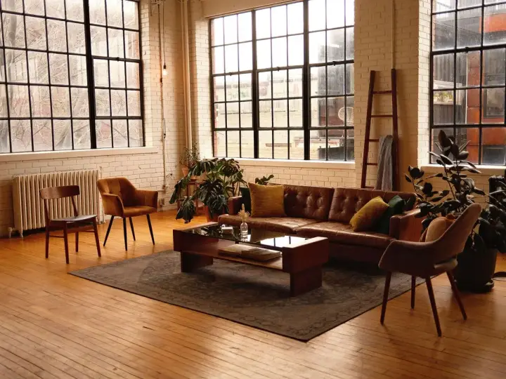 Przytulny salon w stylu loft aranżacje. Brązowa skórzana kanapa, drewniane meble i duże okna tworzą ciepłą atmosferę.