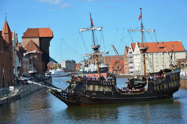 Gdański galeon "Lew" z pasażerami na pokładzie, na tle zabytkowej architektury miasta. To jeden z 7 ciekawych faktów o Polsce, które można odkryć w tym mieście.