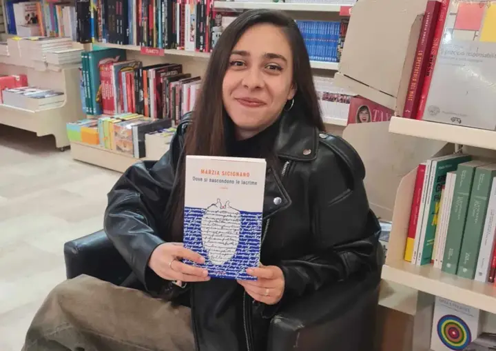 Una giovane donna sorride in libreria, tenendo in mano il libro "Dove si nascondono le lacrime".