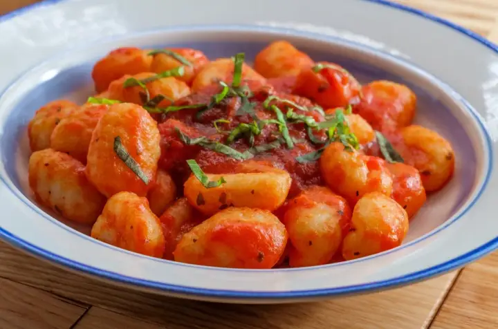 Pyszne gnocchi w sosie pomidorowym, posypane świeżą bazylią, podane w niebiesko-białej misce.