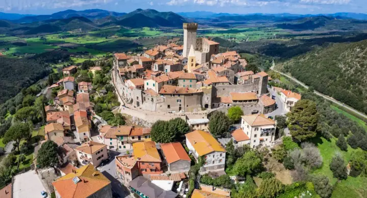 Un borgo medievale con un castello domina le colline toscane. Perfetto per un weekend in Toscana, tra tetti rossi e panorami mozzafiato.