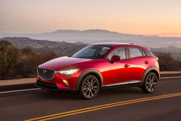 Czerwona Mazda CX-3 na tle górskiego krajobrazu o zachodzie słońca. Elegancka linia nadwozia i lśniący lakier.