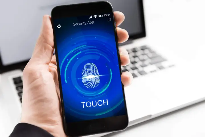Dłoń trzyma smartfon z ekranem blokady "Security App" i ikoną odcisku palca. Proces autoryzacji jest w toku.