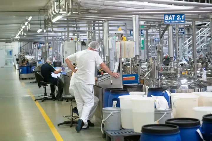Praca w Niemczech z zakwaterowaniem: pracownicy w białych kombinezonach nadzorują produkcję w nowoczesnej fabryce.
