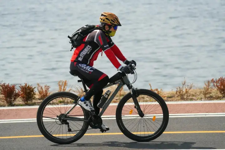 Rowerzysta w kasku i masce jedzie rowerem wzdłuż jeziora. Idealne noclegi dla rowerzystów czekają po wyczerpującej trasie.