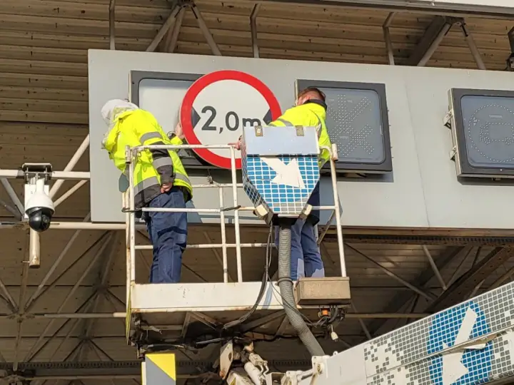 Pracownicy na podnośniku montują znak zakazu 2,0m, pokazując, jak działa e-toll.