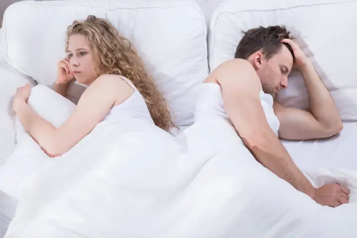 Para, odwróceni do siebie plecami w łóżku, zmartwiona kobieta i mężczyzna z ręką na czole. Czy to pochwica? Co to za problem?