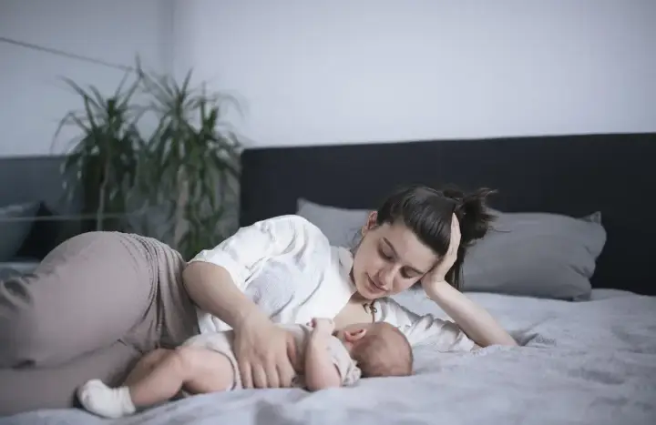 Mama karmi na leżąco swoje dziecko na łóżku. Czuły moment bliskości i spokoju.
