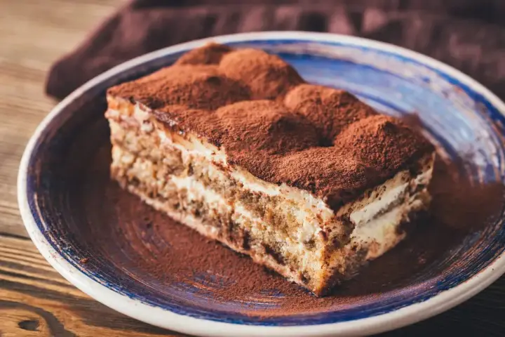 Pyszny kawałek tiramisu z mascarpone, posypany kakao, na talerzu. Idealny sprawdzony przepis na deser.