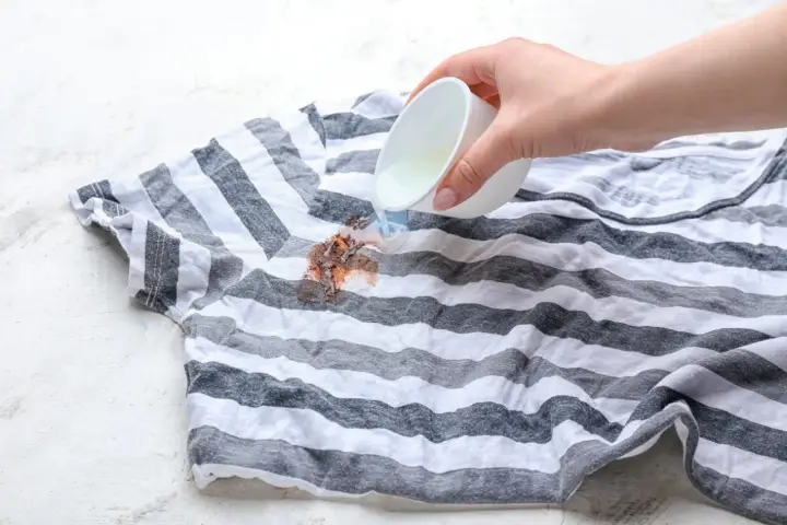 Jak usunąć plamy z czekolady? Płynny środek wylewany na brudny, pasiasty t-shirt.