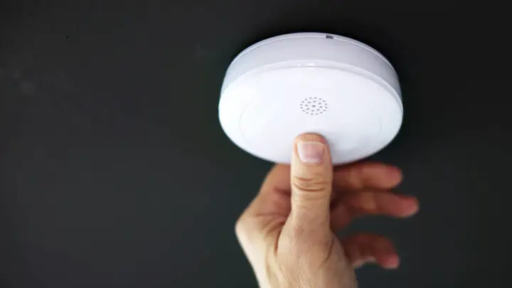 En hand trycker på en brandvarnare som piper trots nytt batteri.