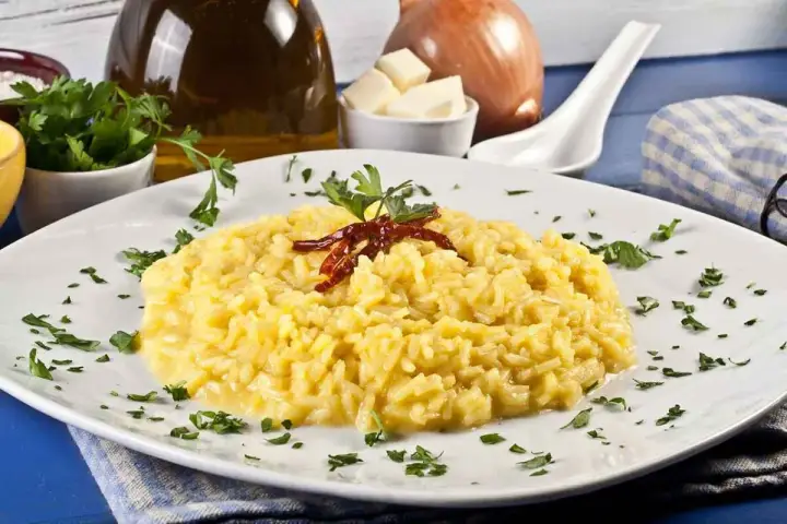 Aksamitne risotto alla milanese, ozdobione suszonymi papryczkami i natką pietruszki, prezentuje się apetycznie na białym talerzu.