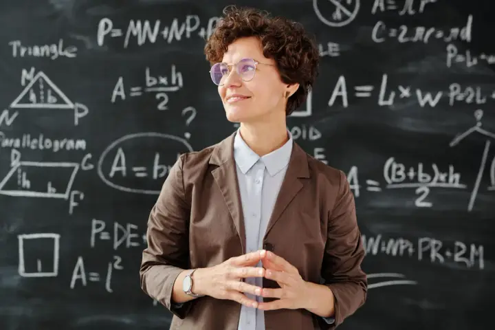 Lehrerin vor Tafel mit Matheformeln. Sie fragt sich, wie viel verdienen Grundschullehrer.