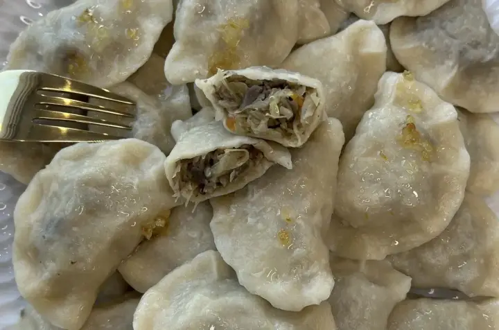 Talerz pełen pysznych, domowych pierogów z kapustą i grzybami. Jeden pieróg jest przekrojony, ukazując bogate nadzienie. Obok leży złoty widelec.