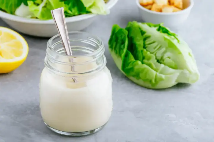 Un pot de vrai sauce césar crémeuse, avec une feuille de laitue romaine et un quartier de citron.