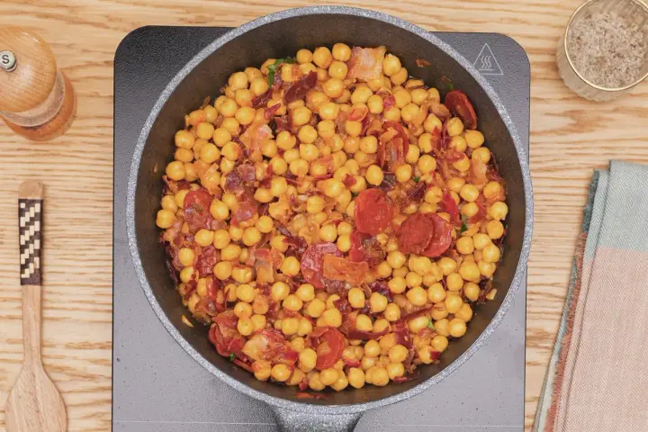 Garbanzos fritos con chorizo y bacon en sartén, listos para servir. Un plato sabroso y reconfortante.