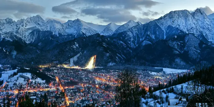 Oświetlone miasto Zakopane nocą, otoczone ośnieżonymi górami. Idealne miejsce na zakup biletów na zimowy wypoczynek.