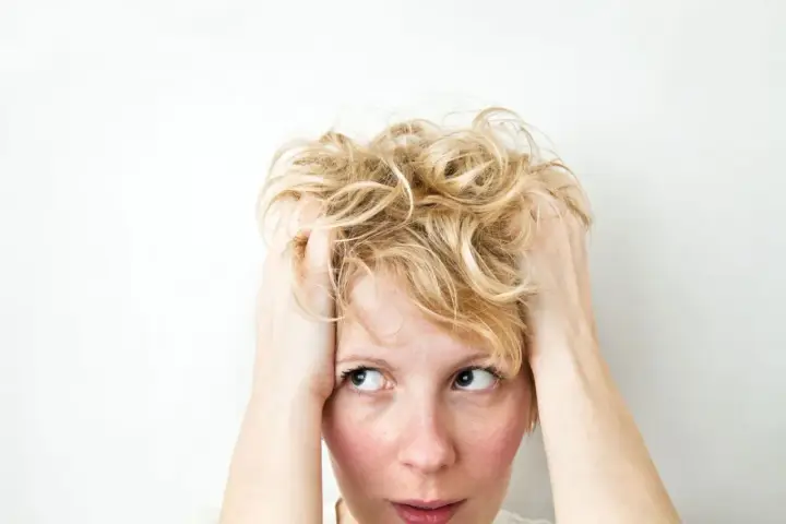 Kobieta z blond włosami, trzymająca się za głowę, z wyrazem zamyślenia i niepokoju, jakby doświadczała wahań nastroju związanych z cyklotymią.