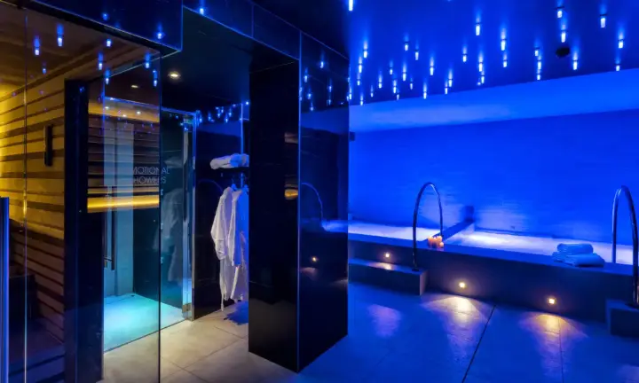 Interni di un centro benessere a Riccione con docce emozionali, vasca idromassaggio e accappatoi bianchi, illuminati da luci blu soffuse.