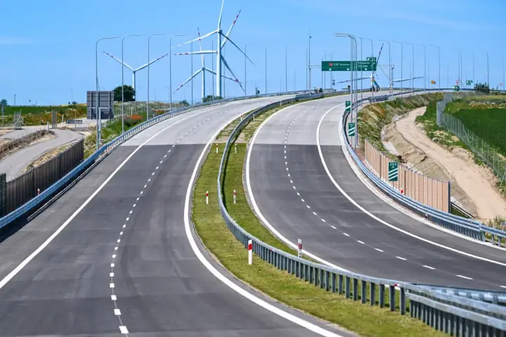 Nowa droga S6 z wiatrakami w tle. Pusta autostrada z zielonym pasem zieleni i barierami.