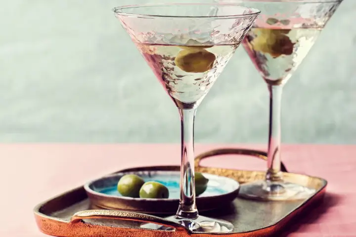 Dwa eleganckie kieliszki z domowymi drinkami z martini, ozdobione oliwkami, na tacy z przekąskami.