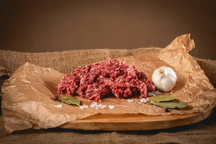 Surowe mielone mięso, idealne na soczyste burgery. Obok czosnek, liście laurowe i sól.