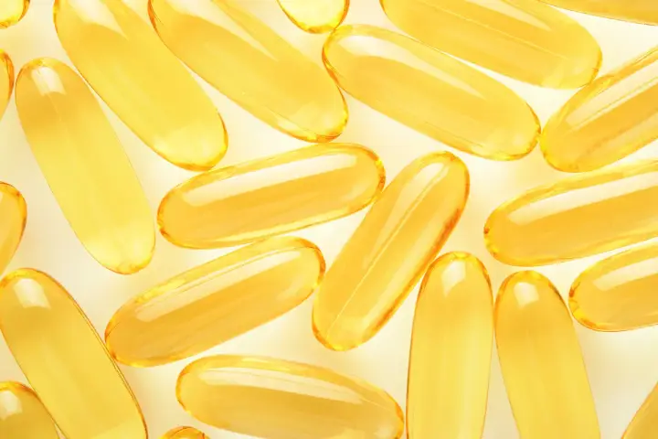 Żółte kapsułki omega 3 ułożone na jasnym tle. Kiedy brać omega 3? Najlepiej po posiłku, by zwiększyć wchłanianie.