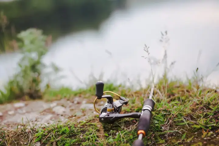 Wędka i kołowrotek leżą na trawie nad wodą, gotowe do połowu. Czas na tarło ryb!