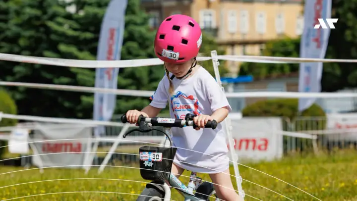 Dziewczynka w różowym kasku na rowerze, z numerem 30. Czy kask na rower dla dziecka jest obowiązkowy? Tak, dla bezpieczeństwa!